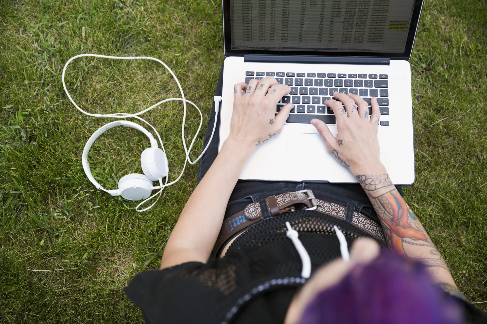 Young woman with tattoos using laptop in the grass